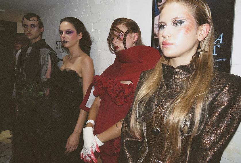 Three models stand together wearing pieces from a collection