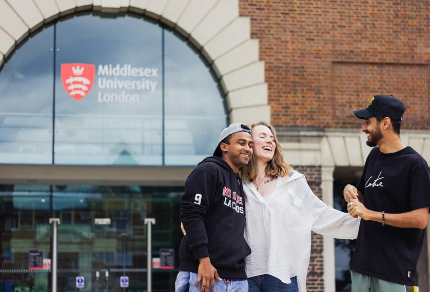 A group of students standing and laughing together outside Middlesex University entrance