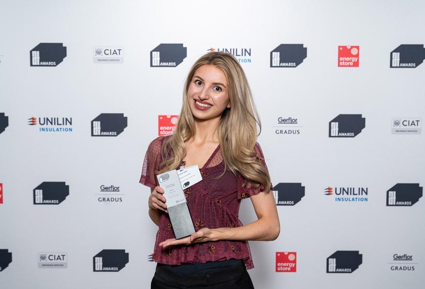 A young Middlesex graduate in a red top holding an award and smiling