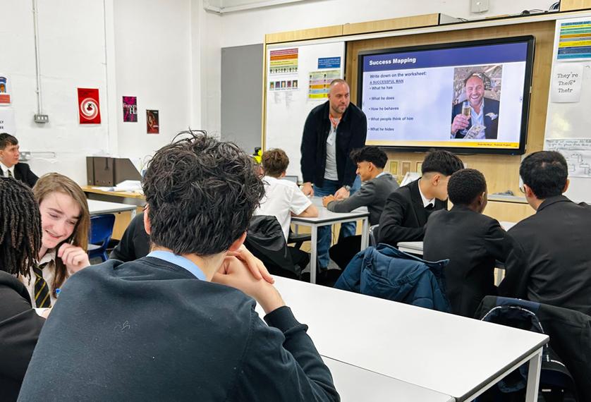Male school pupils in a classroom watching an adult male standing up at a whiteboard