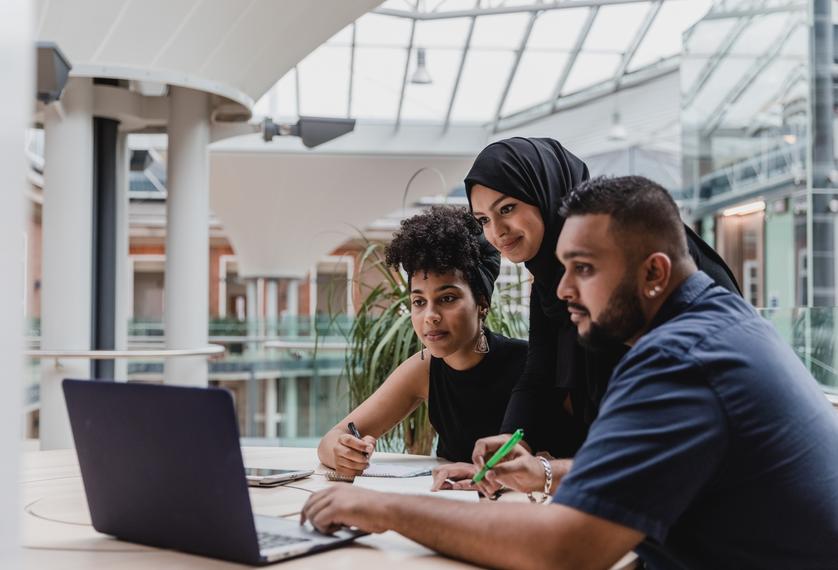 three people look at a laptop