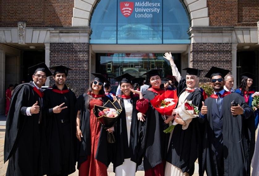 A group of enrobed graduates celebrating in front of the main Middlesex University London entrance