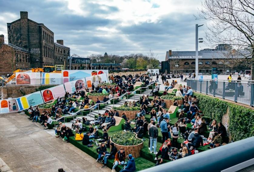A group of individuals sitting on the grass in front of a building at Kings Cross Coal Drops Yard.