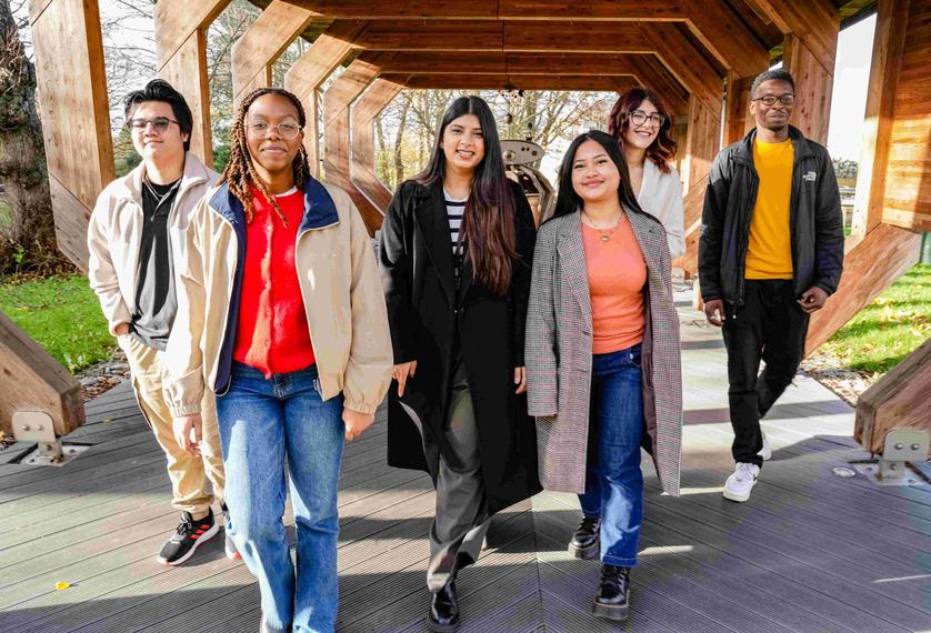 Six students walking together under a wooden structure
