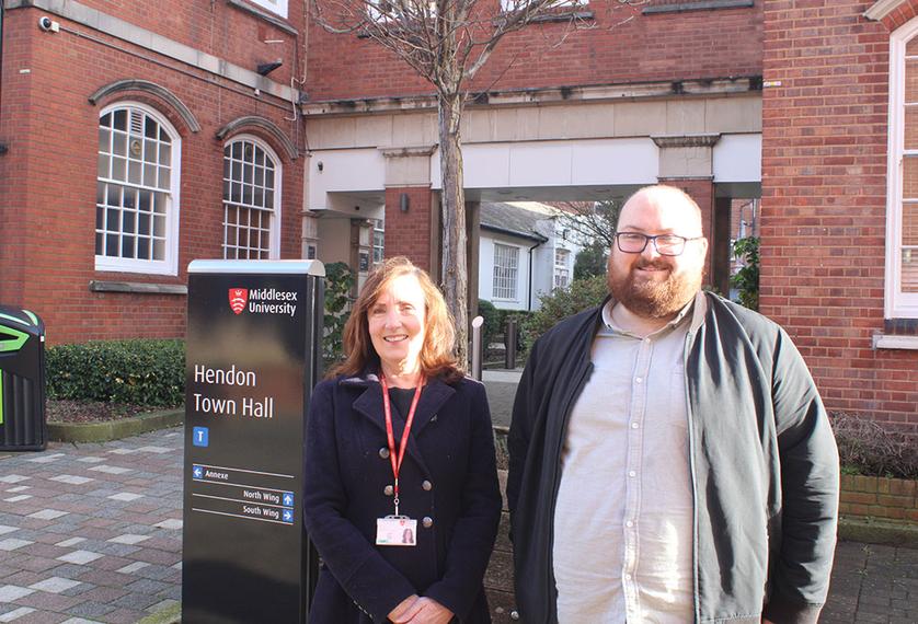 Two people stand next to a university sign