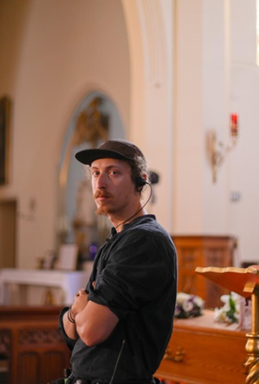 A production design student wearing black with earphones in, at a film set in a church