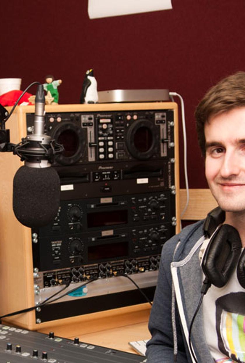 Male student wearing headphones sitting in front of a music mixer device