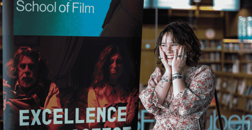 A student standing in front of a banner School of Film