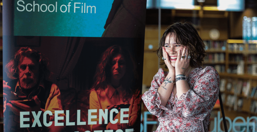 A student standing in front of a banner School of Film