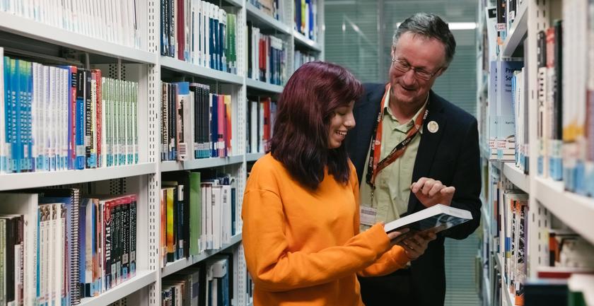 A man and woman in a library, engrossed in books.