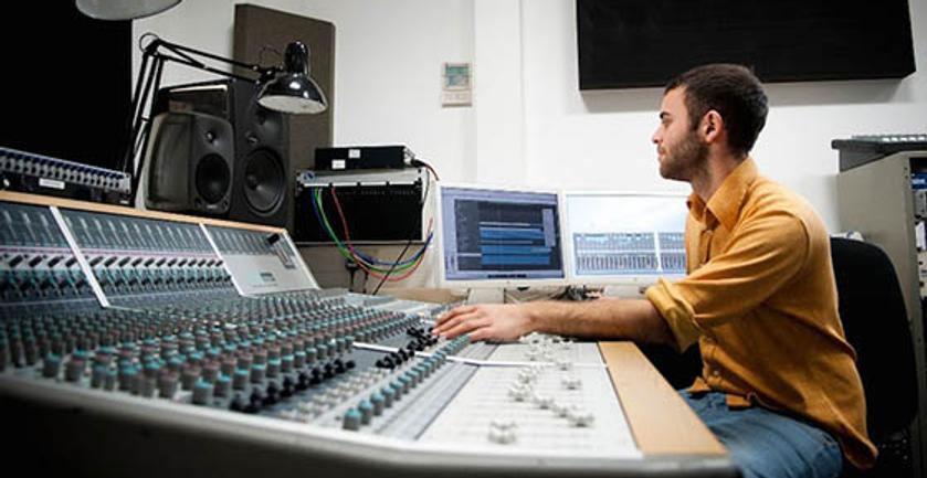 A man sits at a recording studio's mixing desk, adjusting audio levels for a sound production.
