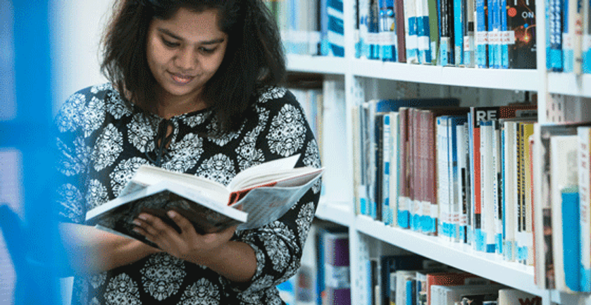 A woman engrossed in reading a book amidst the serene ambiance of a library.