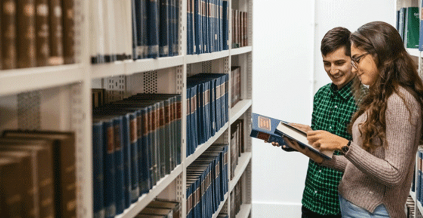Two students in a library, engrossed in books, conducting research for their studies.