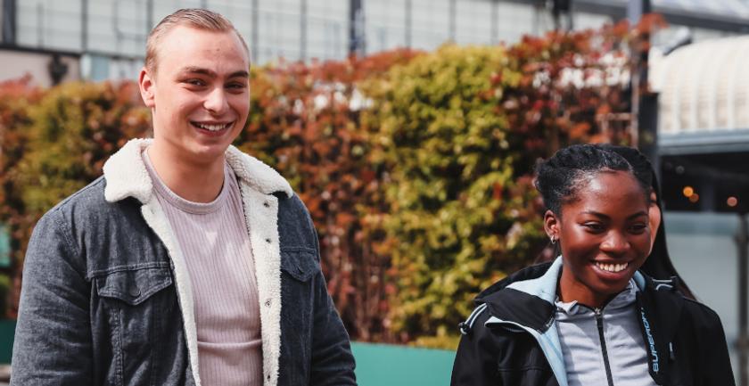 Two young people happily walking side by side, wearing casual clothes and smiling at each other.