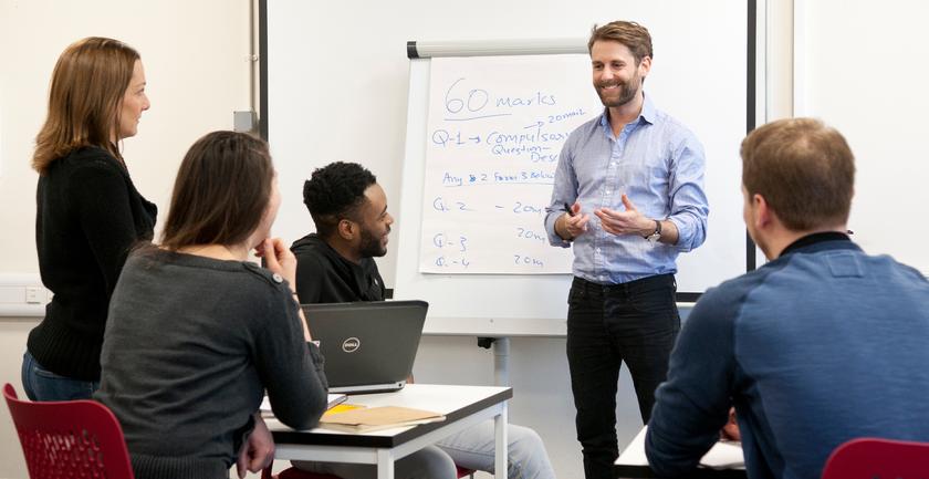 Man standing against a white board talking to students