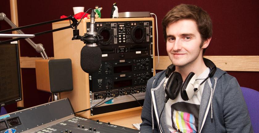 Male student wearing headphones sitting in front of a music mixer device