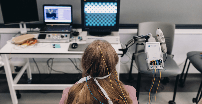A woman sits at a computer with a robotic arm in a healthcare-science lab, demonstrating the integration of technology in medical research.