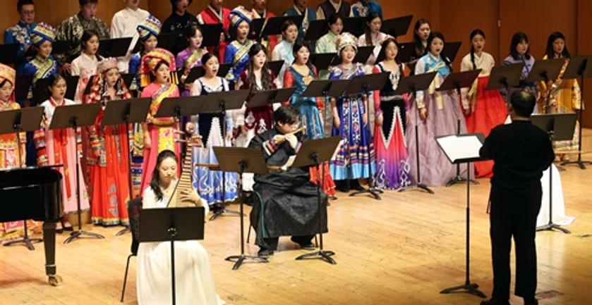 A group of Hainan students performing in a musical orchestra and choir on a stage