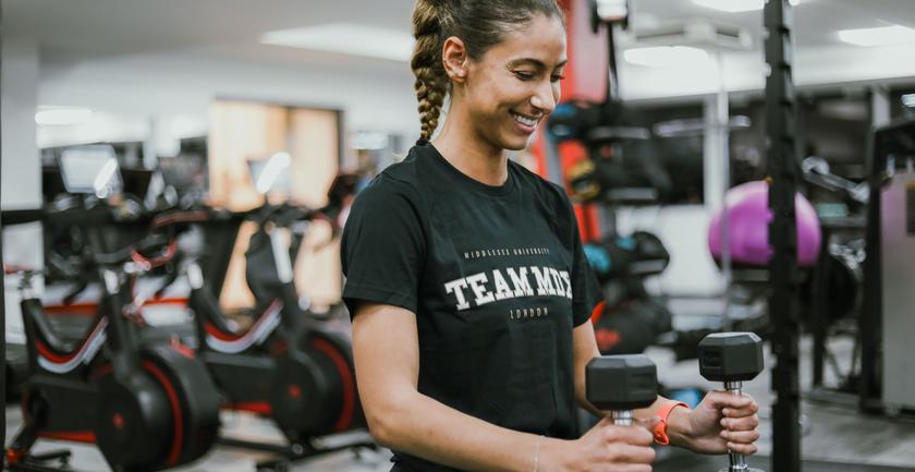 A gym goer smiling with a dumbell in their hand, in the Fitness Pod.
