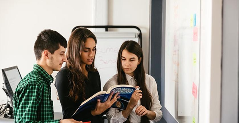 three students study book in front of white board