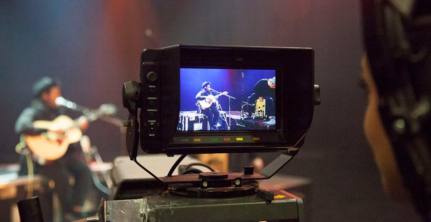 student looks in camera monitor filming musician with guitar