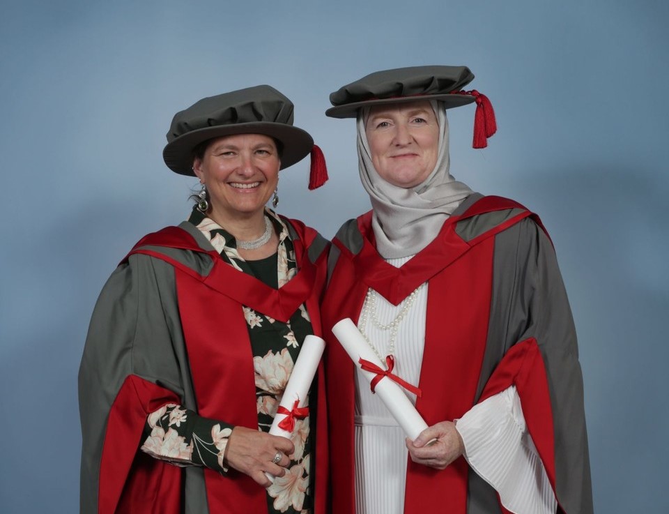 Picture of Dr Lindsay Simmonds & Julie Siddiqi MBE during Graduation in 2024. Both are standing next to each other with professional photography background.
