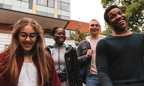 Four smiling students walking down the stairs in front of The Grove, a tall modern building