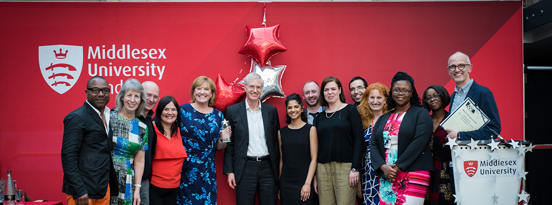 A diverse group of individuals standing together in front of a vibrant red banner.