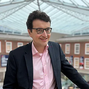 A smiling James Smith on a mezzanine inside the College Building, a red-brick building with a glass ceiling.