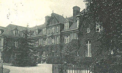 An old, black and white photo of a grand, three-floor building with ivy on its facade