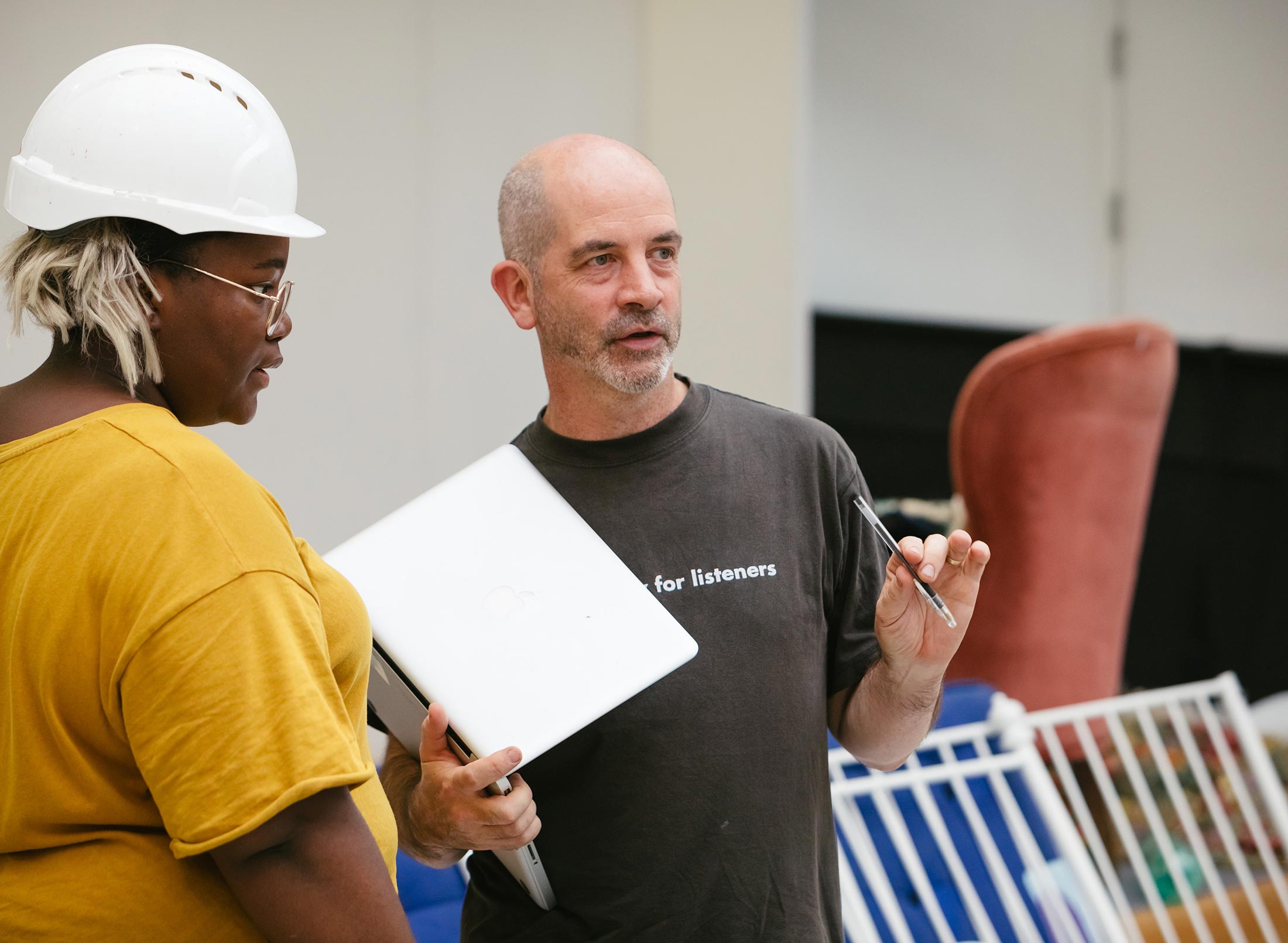 A man and a woman wearing hard hats engaged in a discussion at a construction site.