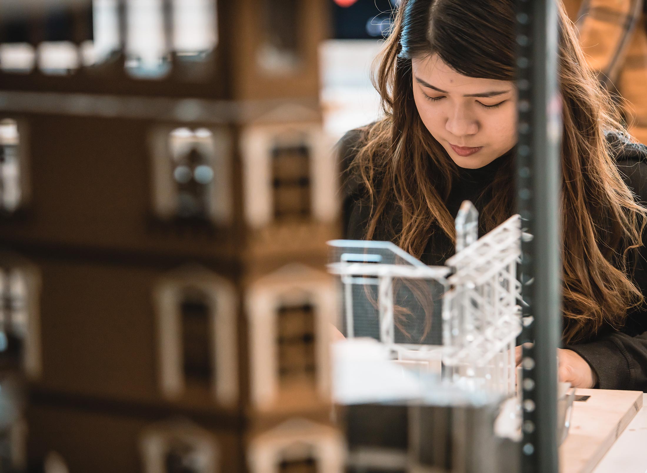 A woman carefully constructing a miniature model of a building using various tools and materials.