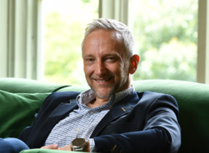 A portrait of Jeremy Chapman sitting in an easy chair in front of a window