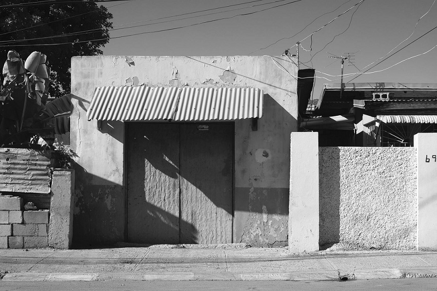 A black and white photo of a one-storey building in Kingston, Jamaica. The building has large doors and an awning, and the photo has been taken in bright sunshine