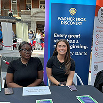 Two ladies representing Warner Bros Discovery, at a stall during a Career fair.