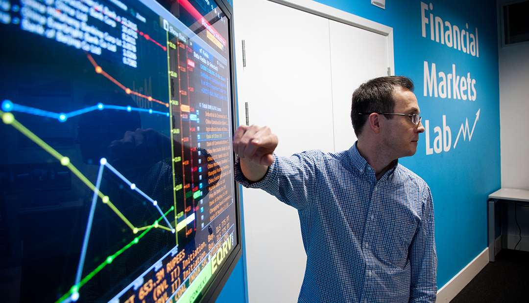 Lecturer gestures to large screen showing financial data