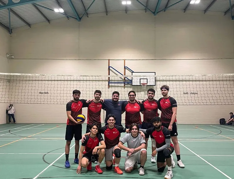 A diverse group of individuals smiling and posing for a photo in a gym, showcasing unity and teamwork in a fitness setting.