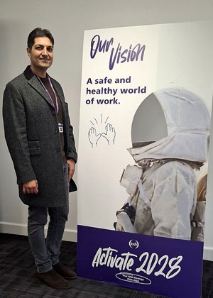 Saeed Ahmadi standing in front of a project board displaying the vision: “A safe and healthy world of work”.