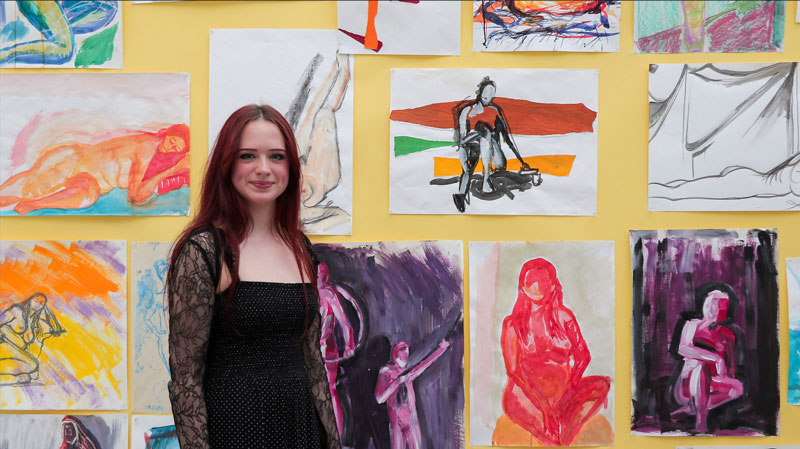Student smiling in front of artwork display.