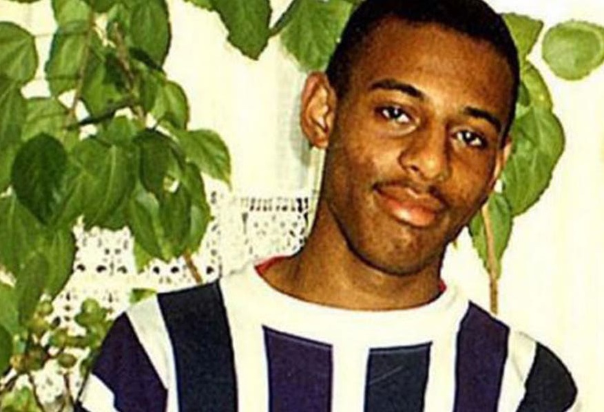 A young man wearing a striped shirt next to a plant