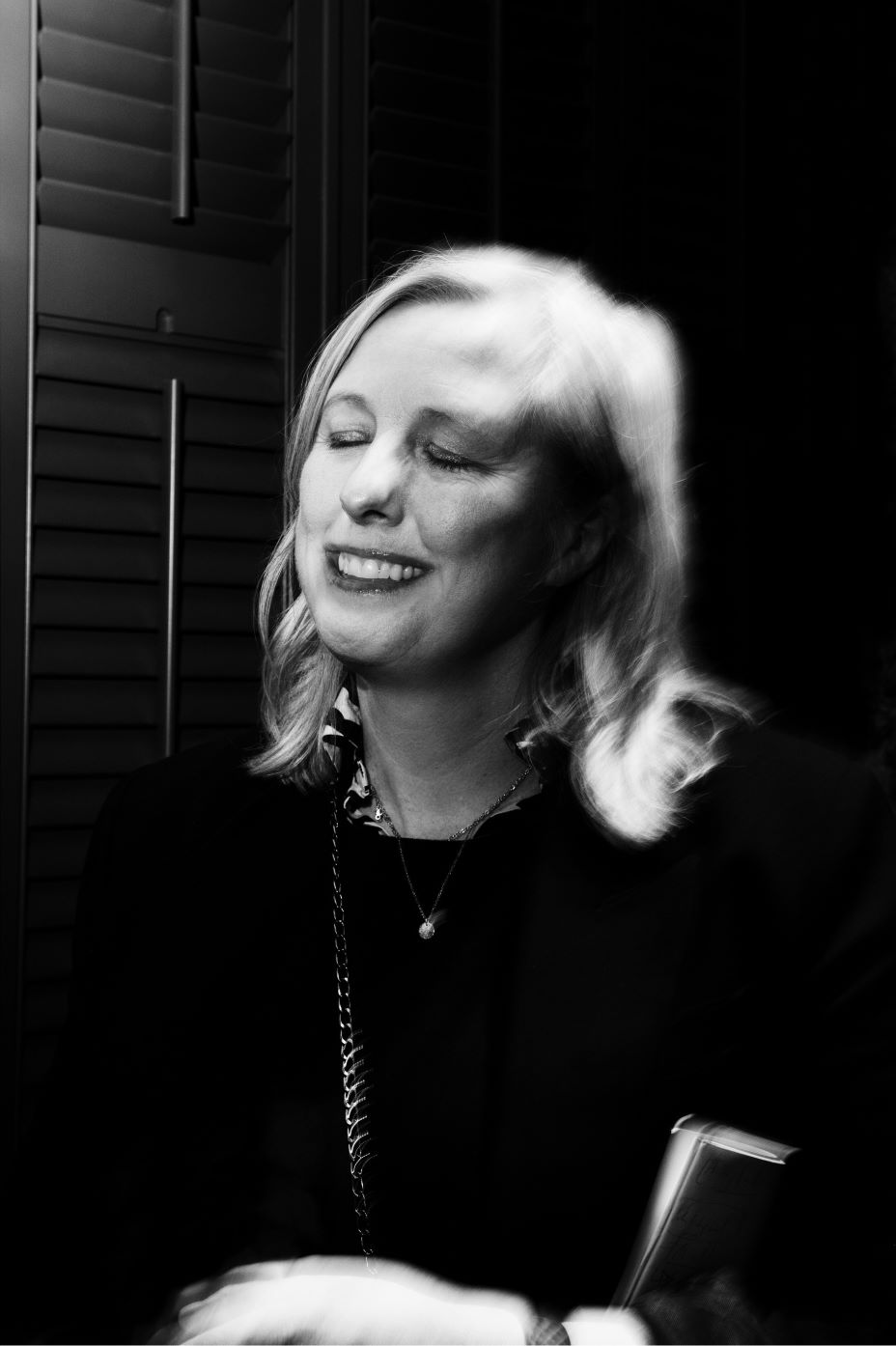 Black and white photo of middle aged white blonde woman, in smart clothes, with her eyes closed. She is smiling