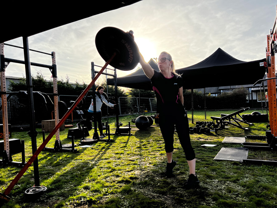 A woman in black sports kit exercises with a large weight in an outdoor gym, in wintry conditions