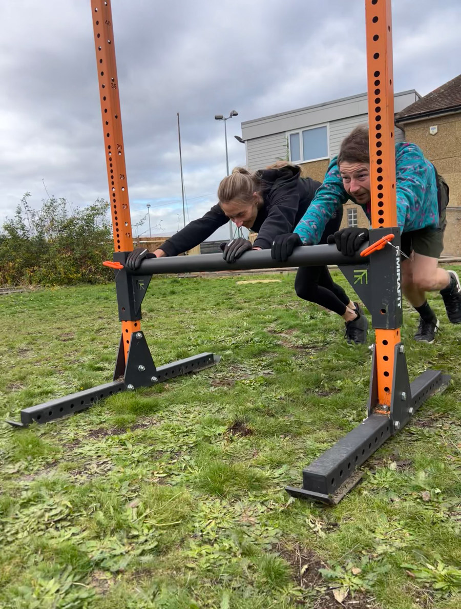 A man and a woman exercise by pushing against a bar in an outdoor gym, in wintry conditions