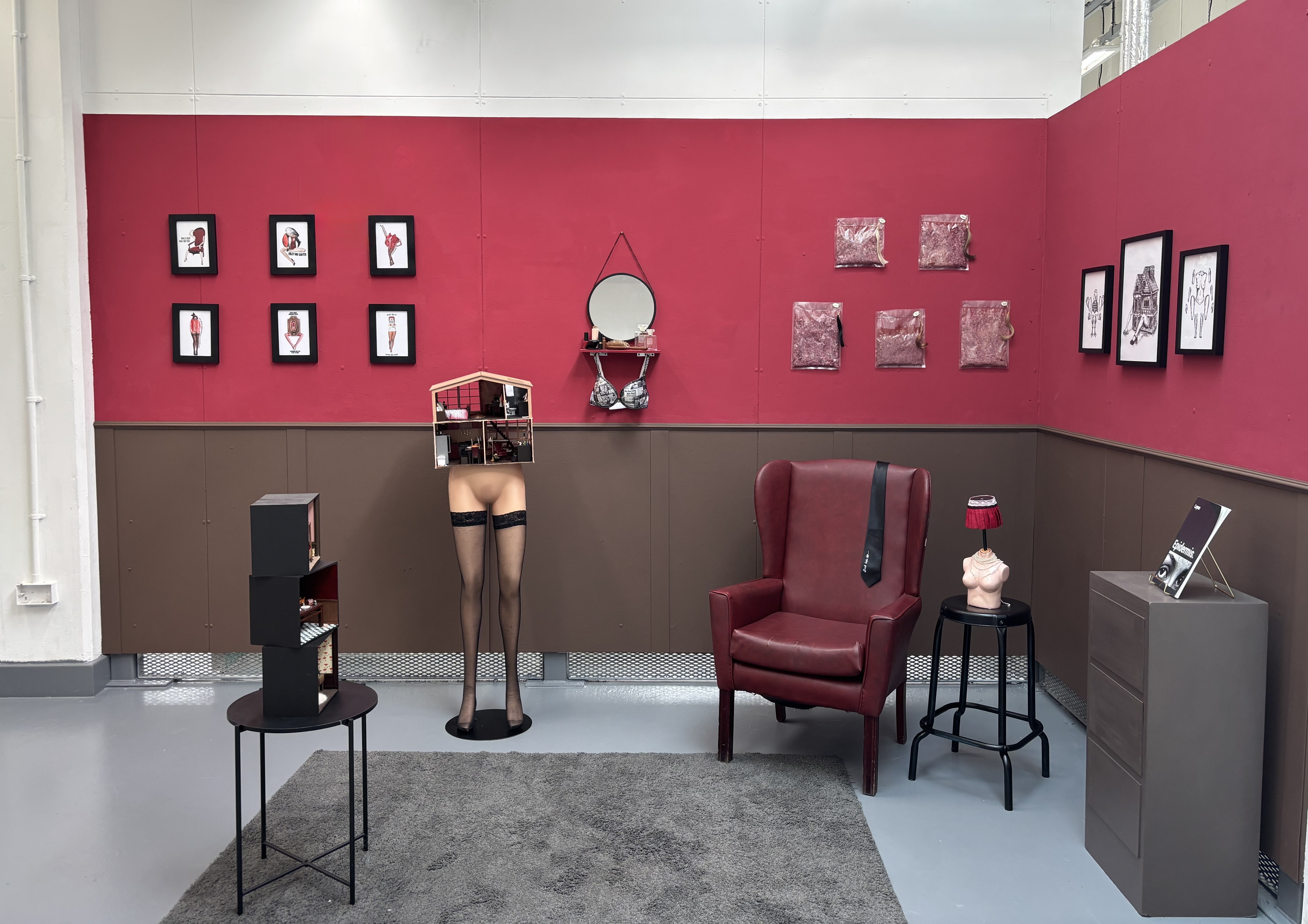 An art installation with red and brown walls on two sides and the legs of a mannequin in the middle with a doll's house instead of a body