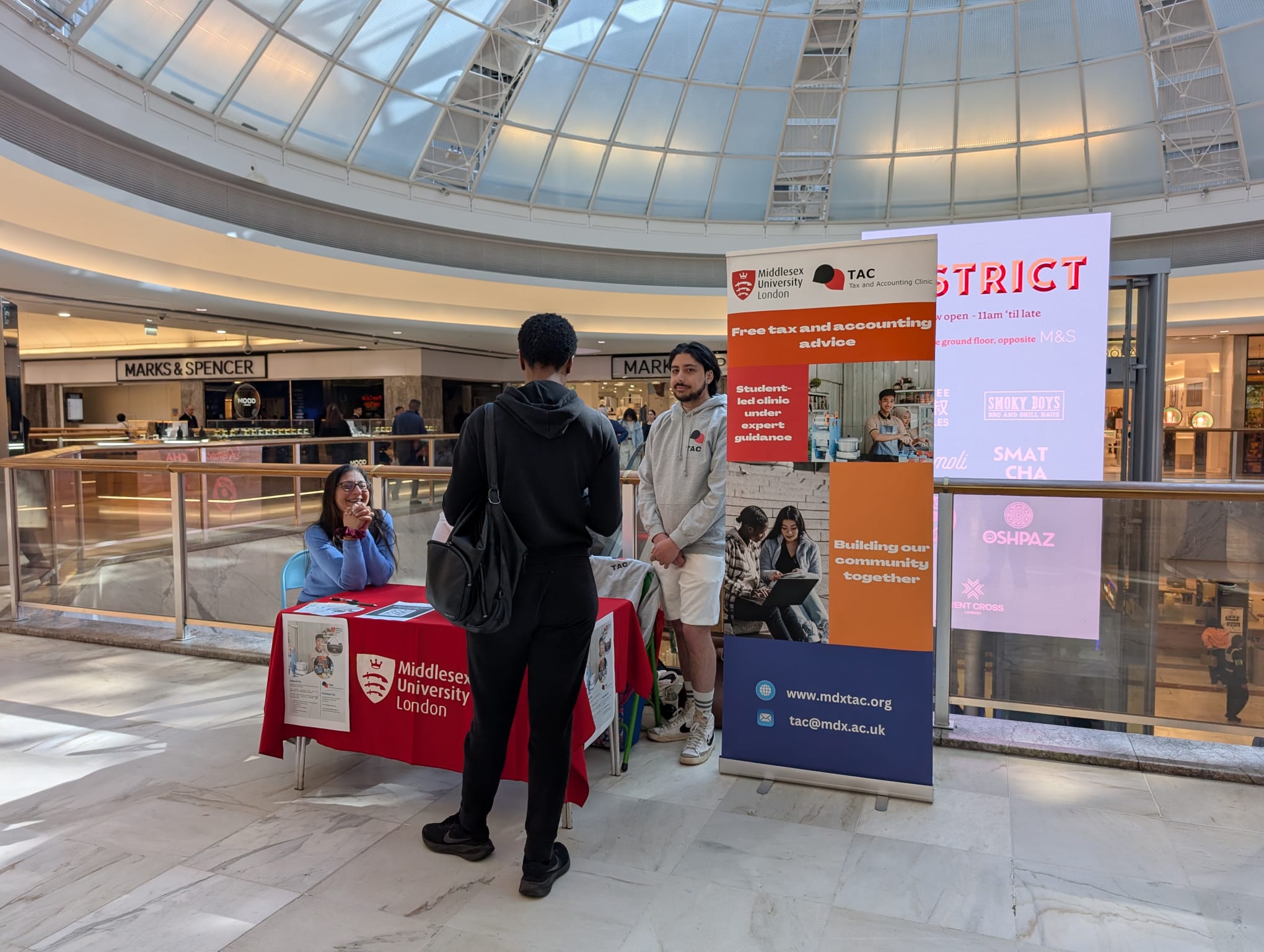 A person speaks to students at a stand in a shopping centre