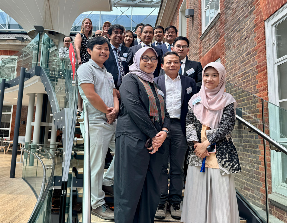 A large group of 15-20 men and women, many from South East Asia, stand on a staircase in the Quad at MDX