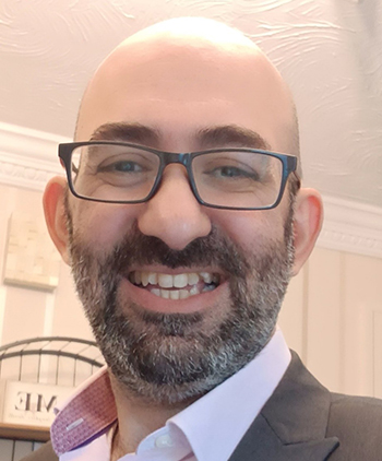 A bald man with glasses smiles at the camera