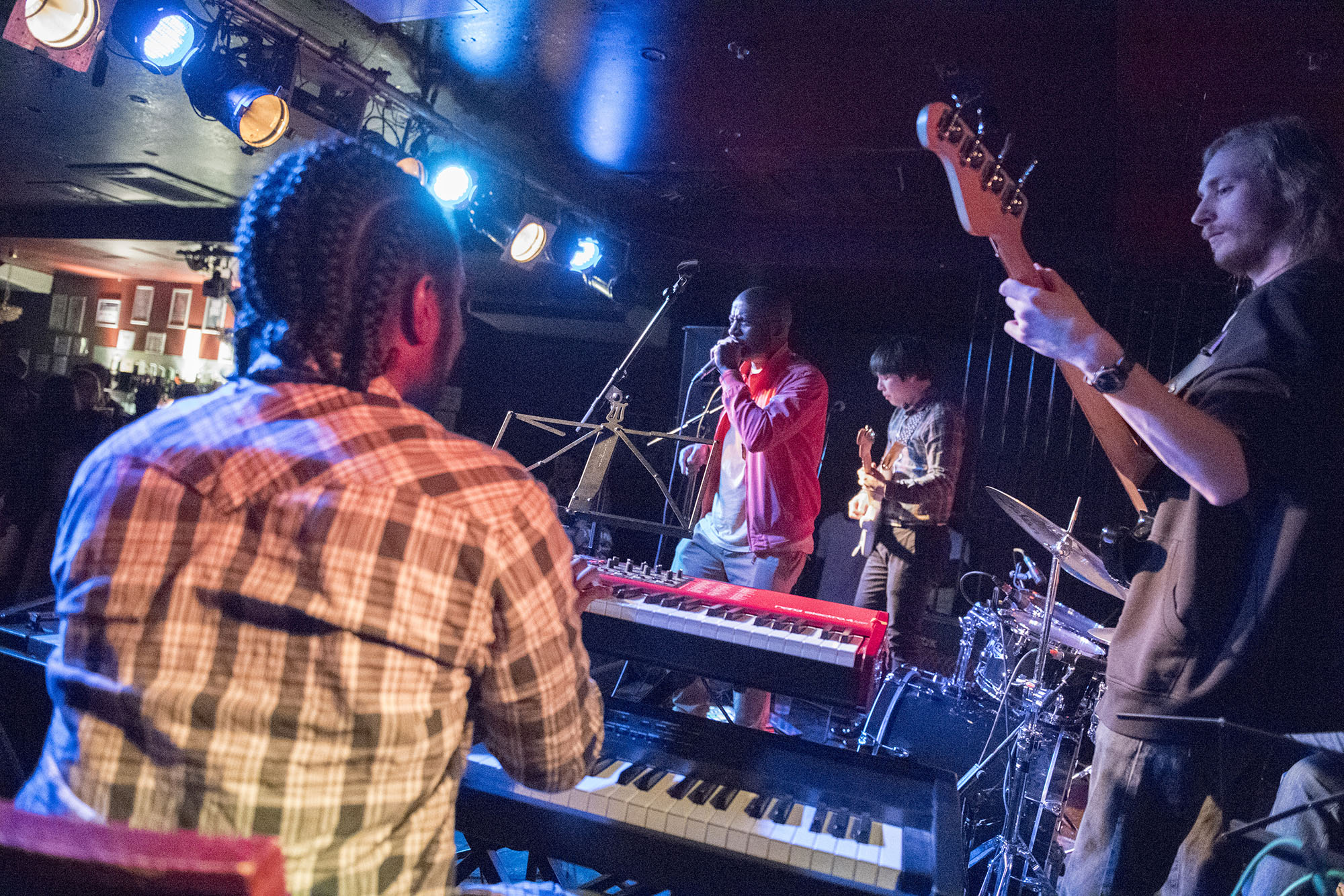 Shot of band playing live show, with keyboardist, bass guitarist, guitarist and singer