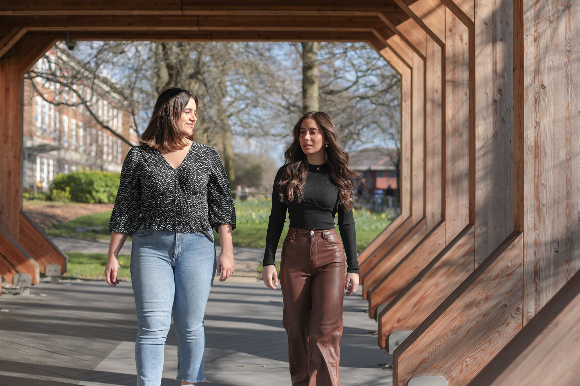 two students walking under wooden structure on sunny day