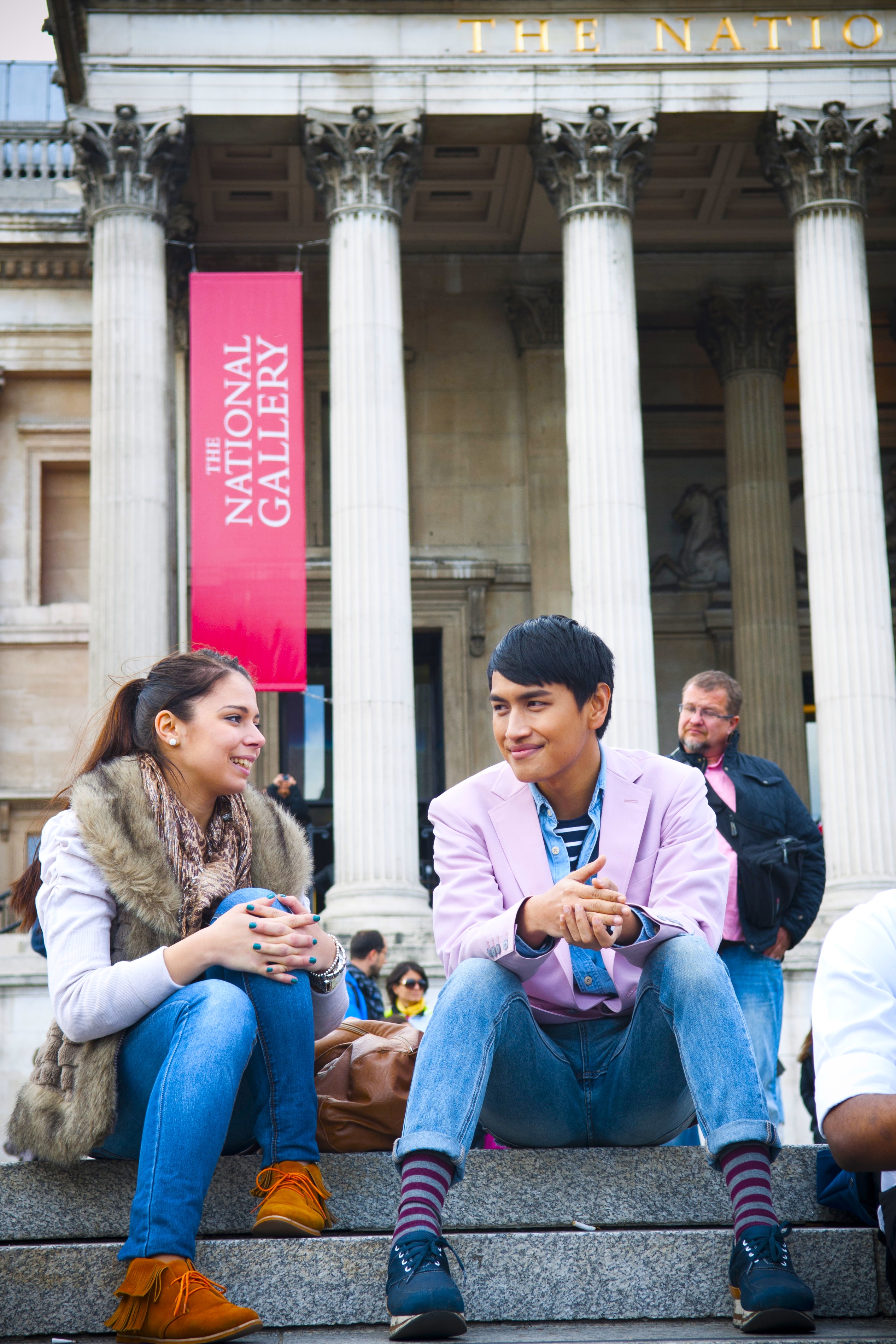 two middlesex students, one male and one female, sit on the steps with the national gallery in the background